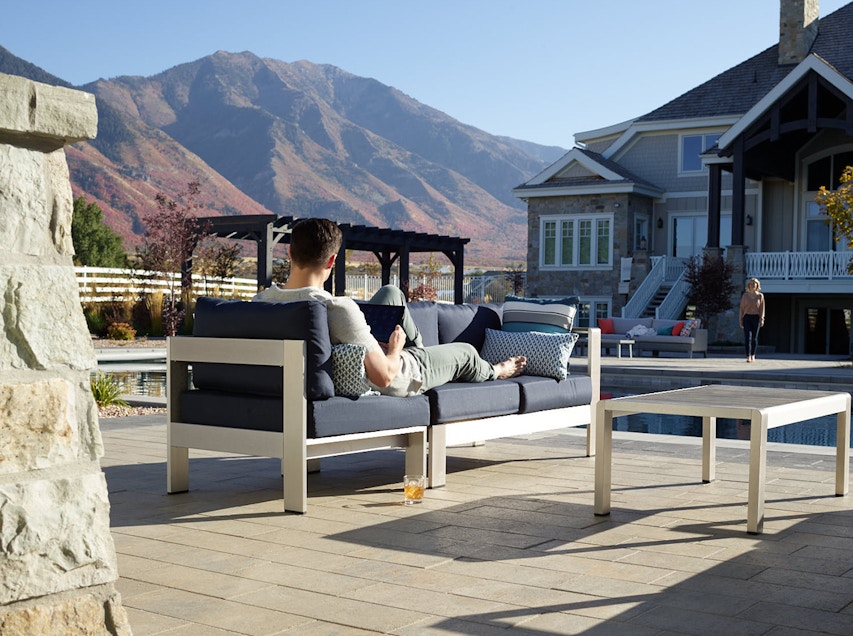 man relaxing beside a pool on a Belgard patio