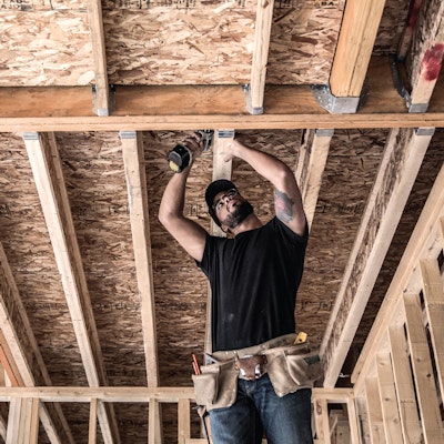 man working overhead in framed house