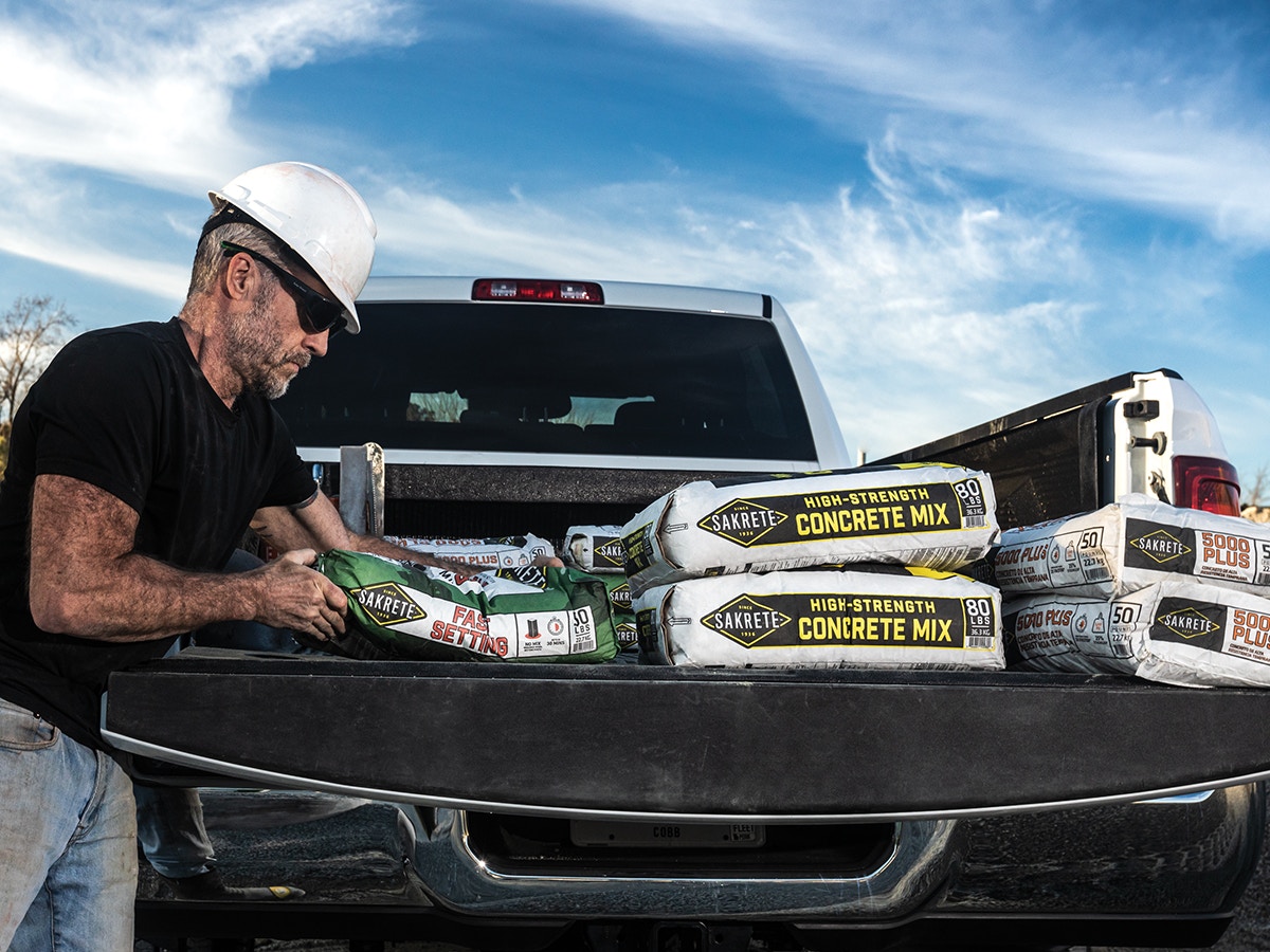 man unloading truck bed full of bagged sakrete concrete