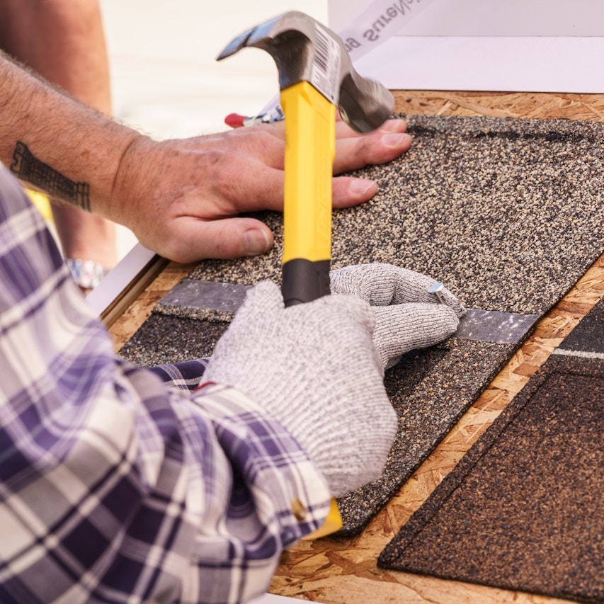 person with hammer and roofing nail, nailing into an Owens Corning shingle