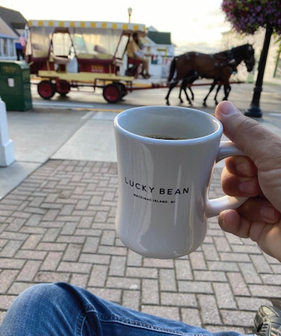 person with coffee cup watching horse and buggy on Machinac Island