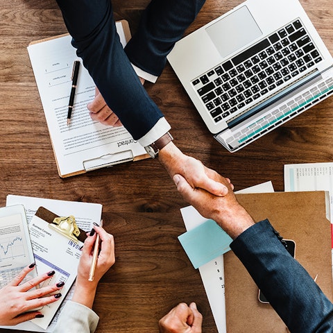 business people shaking hands over a table covered with computers and papers